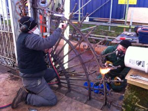 Conservation Blacksmiths using oxy-propane torches and wire brushes to clean back to original surfaces.